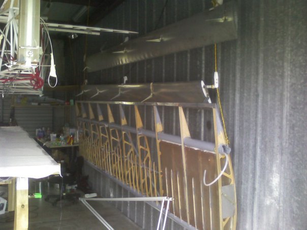Wing and flapperons hanging on the wall with the hanging shelves and hanging fuselage.  The only thing firmly on the earth are the saw horses.
